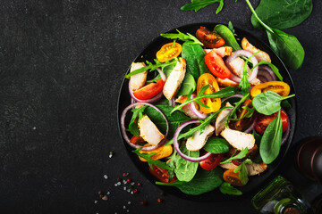 Healthy salad with spinach, grilled chicken, tomatoes, arugula and red onion. Black table, copy space