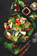 Healthy salad with spinach, grilled chicken, tomatoes, arugula and red onion. Black table, copy space