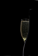 a glass of champagne on a dark background with a silhouette of a bottle