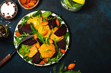 Beet Salad with orange, arugula and almonds on blue table background. Vegan healthy food. Copy space