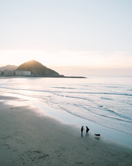 Couple talking on the shore of Zurriola Beach in San Sebastian during sunset while their dog is running around