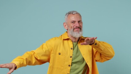 Happy fun elderly gray-haired bearded man 50s wears yellow shirt dance clenching fists waving rising expressive gesticulating hands enjoy isolated on plain pastel light blue background studio portrait