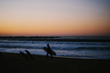 Silhouette of a surfer leaving the beach after the sunset