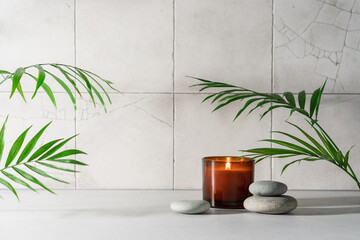 Spa composition with burning candles, zen stones, rolled towels and natural palm leaves. Light stone table and tiles background with empty space for product presentation