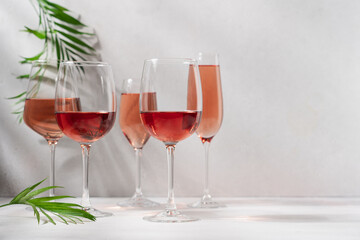 Set of rose wine or champagne in variety of glasses on white background with shadows and palm leaves. Romantic party, vacation, holiday concept
