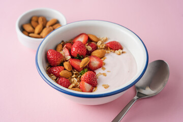 Strawberry yogurt with fresh berries, homemade granola, almonds in bowl. Healthy breakfast on pink background