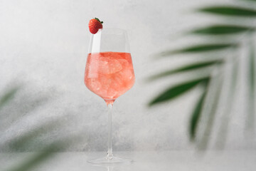 Glass of pink cold cocktail with ice surrounded by palm leaves. Summer refreshing drink on white...