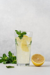 Refreshing lemonade with lemon and mint in glass on light background with copy space. Cold summer drink with ice