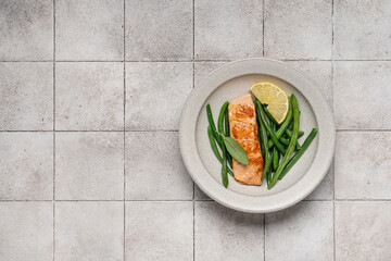 Grilled fried salmon fillet with green bean pods and lemon. Healthy sea food in plate on gray tiled background
