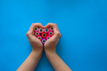 Colorful spools of thread in the shape of a heart hands on on a light blue background. Women's hobby. Sewing concept. Empty space for text.