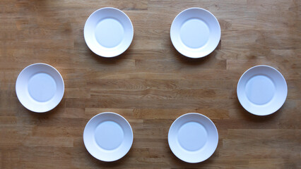 Table set for 6 dinners with empty white plates on a wooden table. The plates can be fulfilled and there is some copy space at the middle of the image.