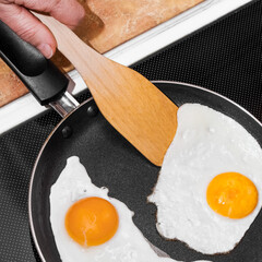 A woman prepares scrambled eggs from two eggs in a frying pan. Morning breakfast concept