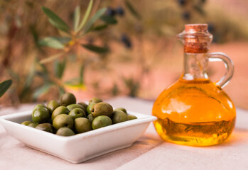 still life of olives and oil on a table against a background of olive trees
