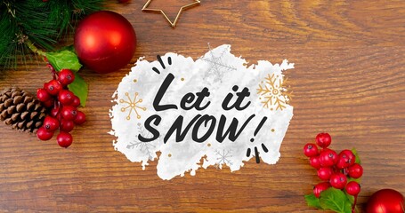 Overhead view of let it snow text over pine cones with baubles and cherries on wooden table