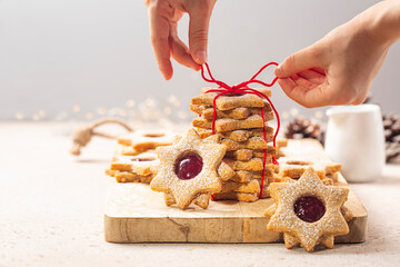 Preparing a cookie gift. Girls hands tying a red  bow cord. Homemade star or flower shaped linzer cookies with raspberry jam. Christmas or mother day present concept. Selective focus.