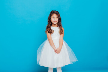 Fototapeta na wymiar a little curly girl in a white princess dress on a blue background