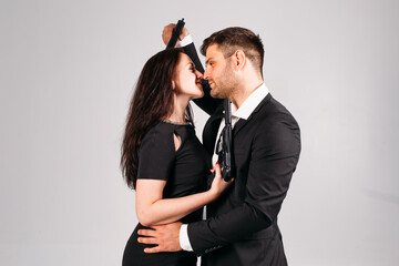 young couple, in black suits with pistols in their hands on a white background in the studio, they depict security guards, bodyguards or agents.