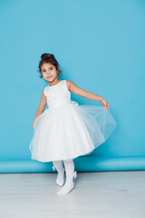 Fototapeta na wymiar a little curly girl in a white princess dress on a blue background