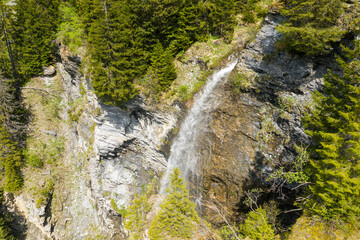 A waterfall at the edge of the lake and the Dam of Saint Guerin in Europe, in France, towards Beaufort, in the Alps, in summer, on a sunny day.