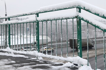 Snow adhered to the metal railing of an aerial pedestrian crossing on the background of cars on the...