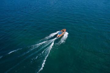 Large classic Italian boat with two men moving fast on the water. Riva Aquarama Classic in motion on the water aerial view. Aquarama special top view.