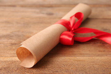 Rolled student's diploma with red ribbon on wooden table, closeup