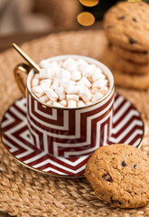 A cup of hot cocoa with marshmallows and american cookies with chocolate drops on wicker straw stand. Close-up.