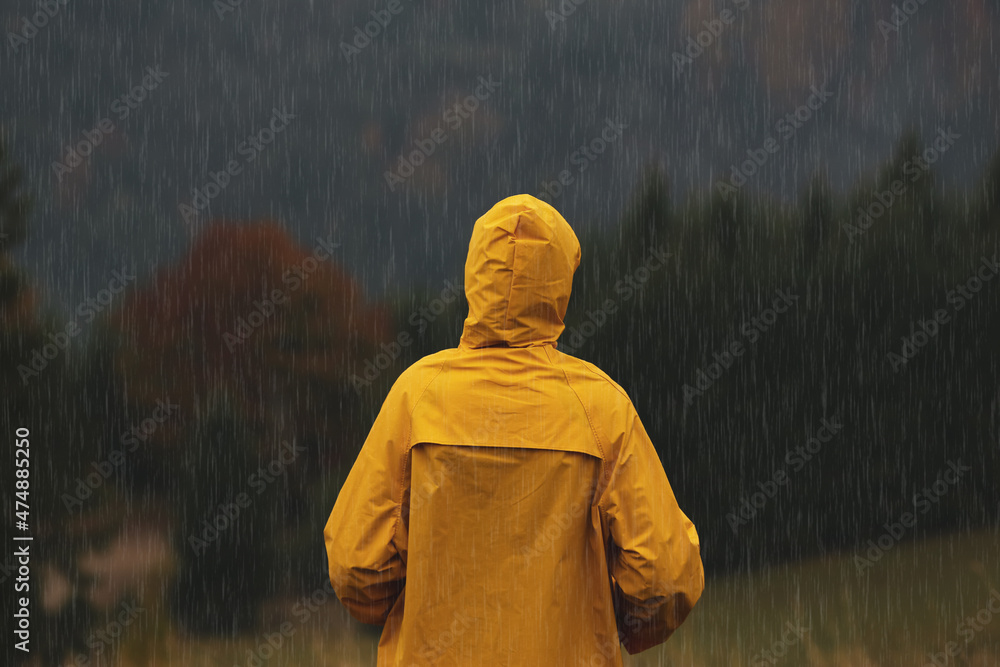 Poster Woman in raincoat enjoying mountain landscape under rain, back view