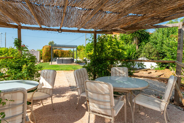 Interior view of a garden gazebo in a relaxing villa hotel, lounge with table, chairs, grass and garden. Mediterranean style