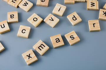 Scattered wooden tiles with letters with visible words - covid, xmas isolated on grey background 