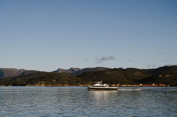 Landscape of hilly area of island in Lusefjord. Boat sails along the fjord. Tourism in Norway. Beautiful nature on sunny day.