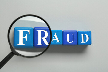 Wooden cubes with word Fraud and magnifying glass on light grey background, flat lay
