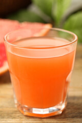 Glass of delicious grapefruit juice on wooden table against blurred background