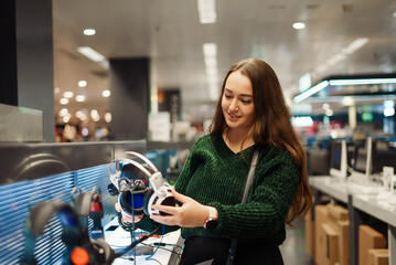 Cheerful young woman buying new headphones in tech store department