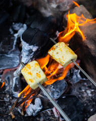 Halloumi cheese is fried over a bonfire, with a beautiful flame.