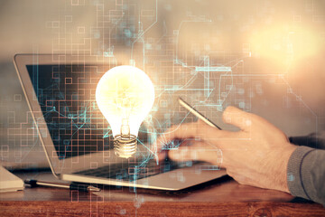 Double exposure of man's hands holding and using a digital device and bulb hologram drawing. Idea concept.