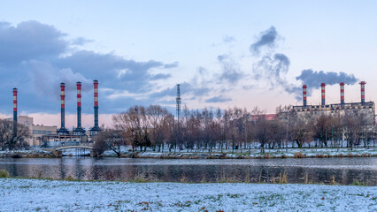 Obraz premium Smoking chimneys of thermal power plants near the waterfront in city. Winter. Industrial and nature background.