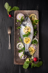 Raw fish on black background and vegetables, top view photo, fork