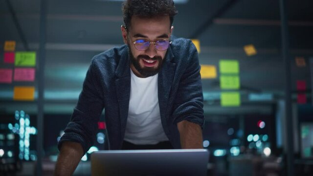 Successful Handsome Disruptive CEO Working on Laptop Computer in Big City Office Late in the Evening. Businessman Preparing Visionary Infrastructure Presentation for Next Board of Directors Meeting.