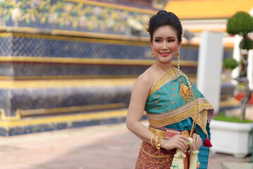Portrait Asian women smiling and wearing Thai national costumes are inside temples to worship Buddha with flower garlands on important religious days for Thai people.