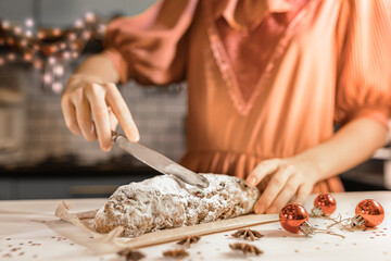 cut festive traditional German Stollen pie into pieces. girl in festive dress cuts stollen with knife in kitchen on christmas eve