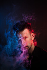 portrait of a young man who exhales a lot of smoke in neon light. red and blue