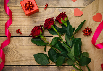 Top view, red gift box. Festive atmosphere, bouquet of red roses and bows on a wooden background.