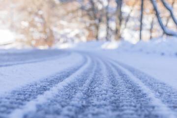 Low angle view on an asphalt road covered with snow leading to a left turn. Trees in the background. Diminishing perspective. Selective focus. Copy space.