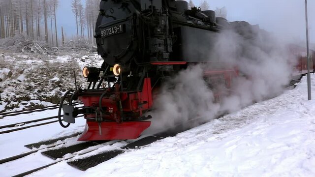 Black steam locomotive in a snowy landscape stands on the rails and pushes steam out over the locomotive brakes