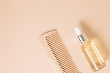 Natural hair care oil and wooden comb on beige background, top view.