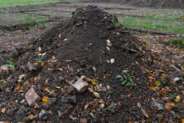 Pile of dark construction gardening soil mud land earth dirt heap pile mound, freshly dug, with some wet soil and leaves
