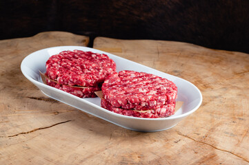 four raw minced meat burgers in a white bowl on wooden table