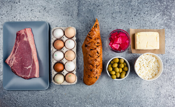 Deli shop assortment of raw beef steak, egg carton, baguette, marinated red cabbage, green olives, butter and bowl of cottage cheese