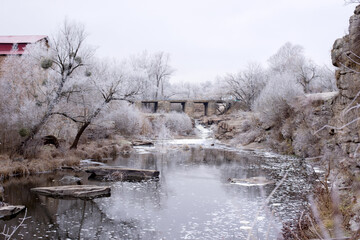 Beautiful winter landscape with Old stone bridge across the Girskiy Tikych river running through frosted trees and rocks.